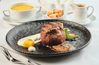 a steak on a plate with a cup of soup