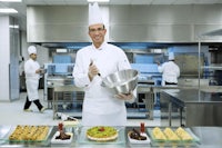 a chef holding a plate of food in a kitchen