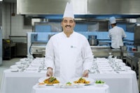 a man in a chef's uniform standing in front of plates of food